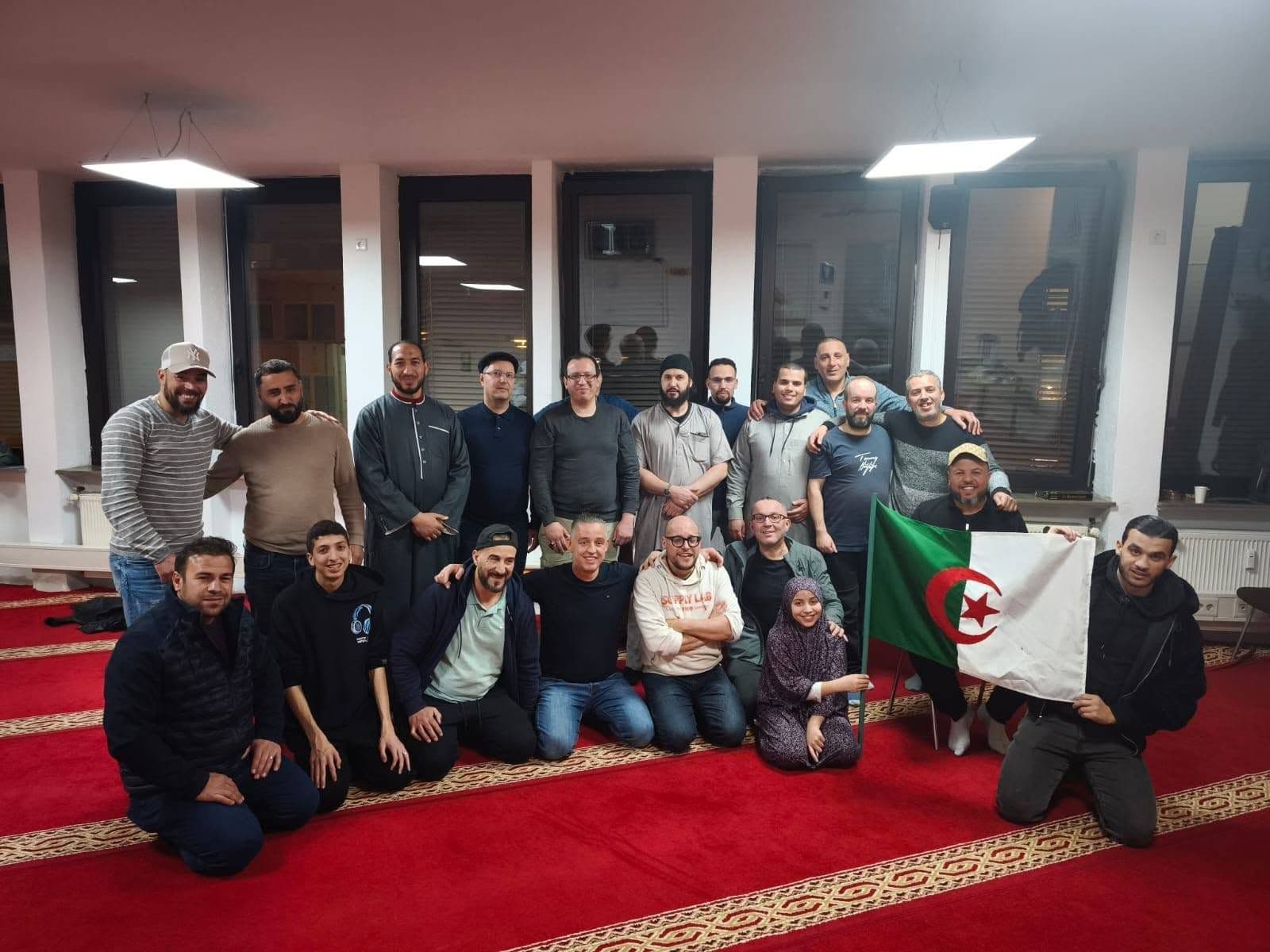 Eine große Gruppe von Mitgliedern mit der algerischen Flagge in einem Saal