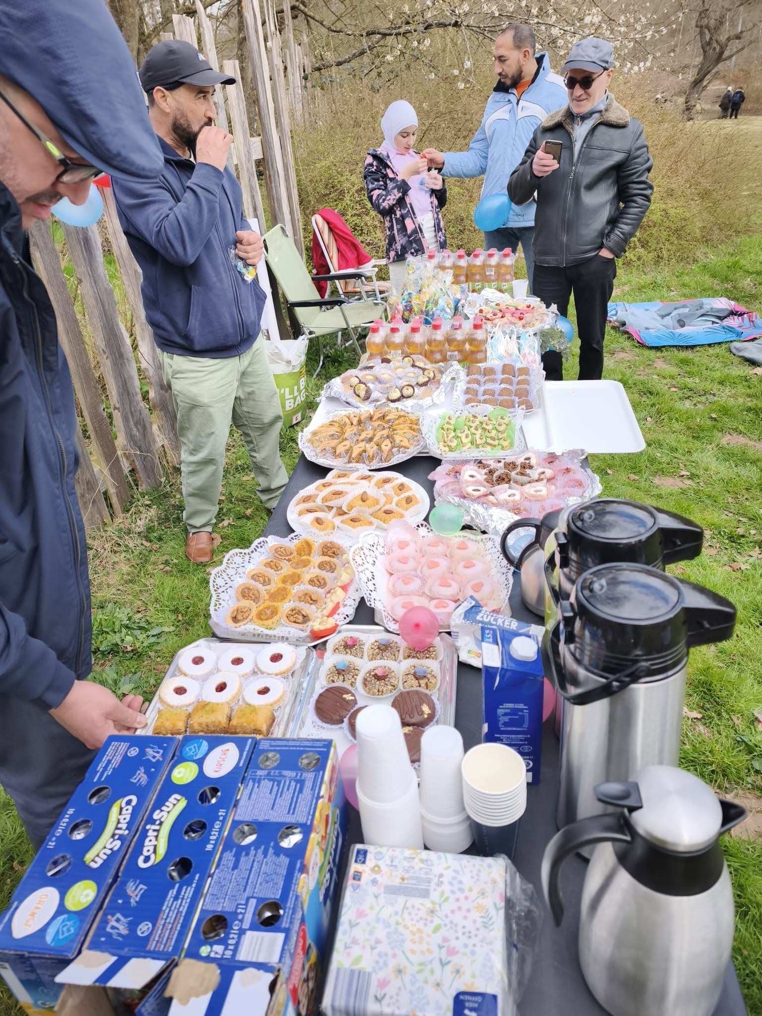 Ein Buffet mit Kuchen und Tee im Freien, Familien im Hintergrund